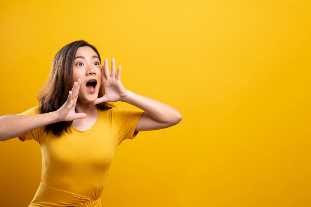 Happy woman making shout gesture isolated over yellow background